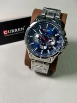 Curren 8363 plateado con esfera azul en un soporte, con su caja